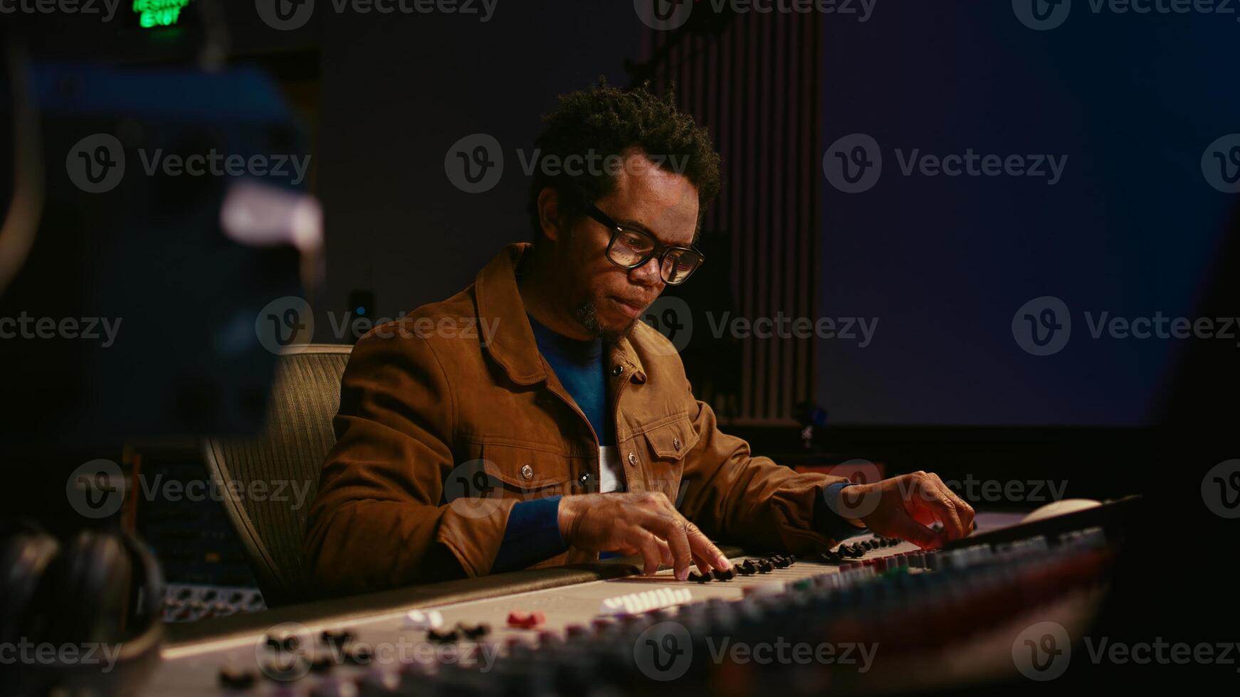 Music producer using audio mixer in professional studio, adjusting volume levels while pressing buttons and sliders on control desk. Sound designer works with digital audio software. Camera A. photo