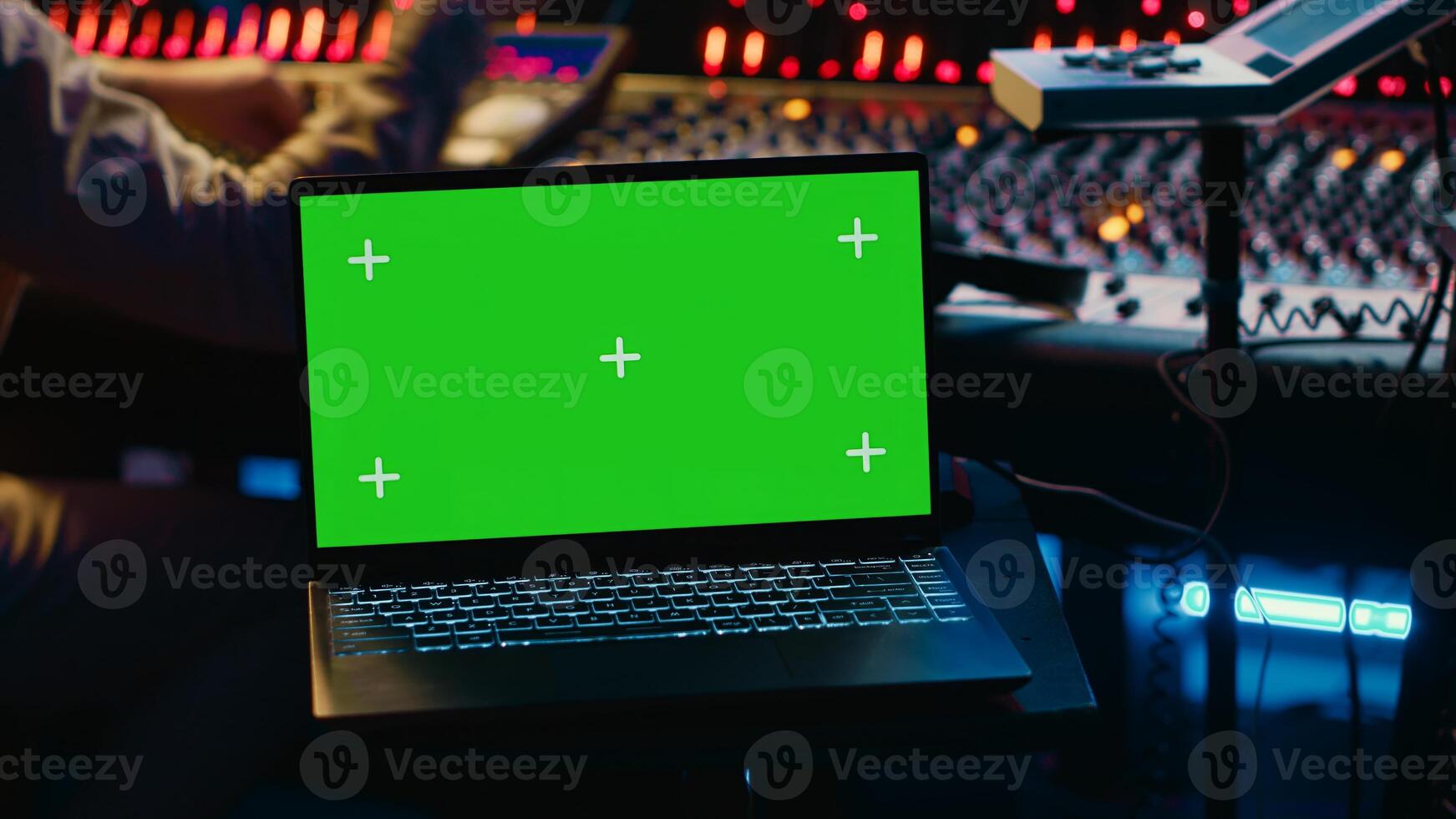 Music production engineer mixing and mastering music in control room, using laptop with greenscreen display. Skilled audio technician working with recording software on pc, pushing faders. Camera A. photo