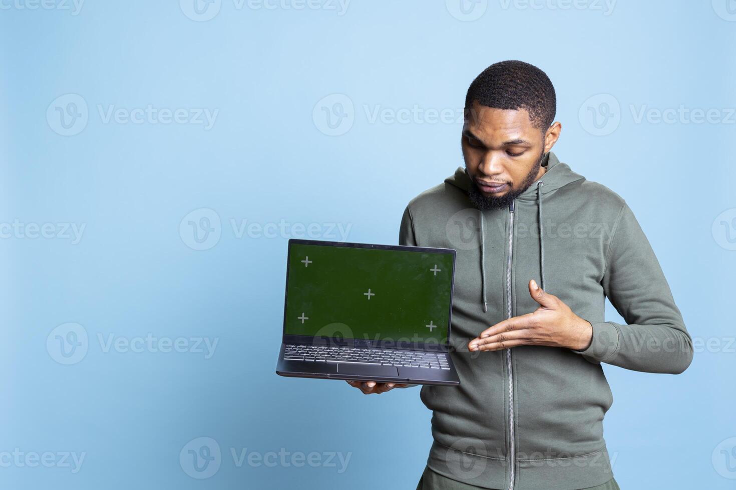 Jolly african american person presenting green screen display on laptop, doing recommendation. Friendly young guy pointing at mockup on notebook, wearing casual clothes in studio. photo