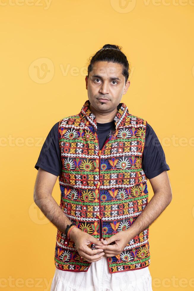Portrait of man wearing colorful vest standing isolated over studio background. Indian person dressed in traditional clothing, feeling satisfied, studio backdrop, camera A photo