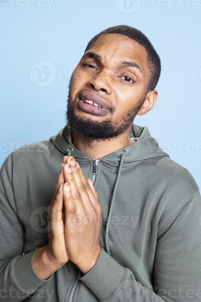 Young sorrowful person begging for something in studio, holding hands in a prayer and beseeching to receive mercy. Appealing in misery and having belief, pleading for forgiveness. photo