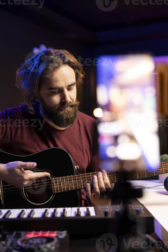 Professional singer teaching guitar lessons online on social media channel, recording himself playing acoustic instrument accords and explaining notes on strings. Young artist making tutorials. photo