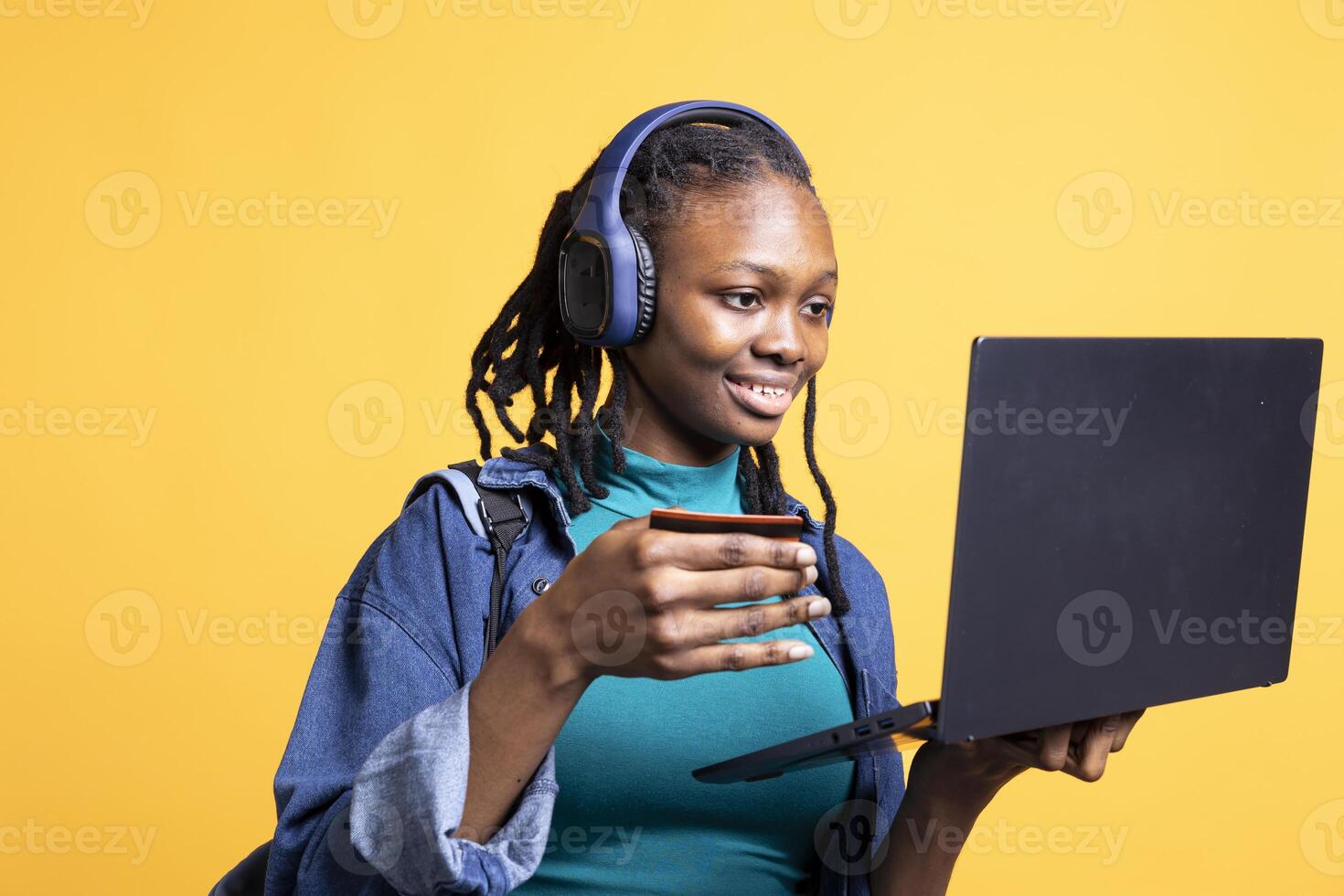 Joyful woman listening music adding payment method on website using laptop, enjoying sales period, studio background. Girl doing financial transactions on internet using credit card on notebook photo