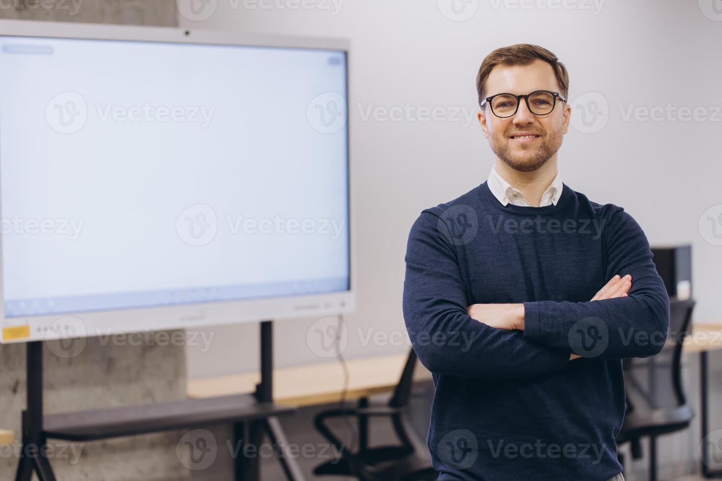 Professional businessman smiling, crossing arms while standing in sleek workspace near blank interactive display screen photo