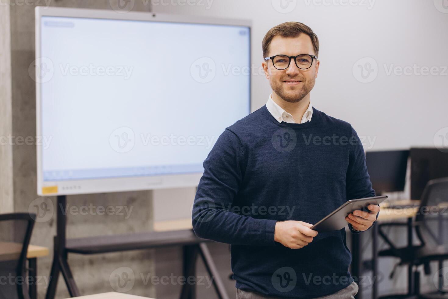 Businessman holding tablet and smiling in modern office with blank interactive whiteboard ready for presentation photo