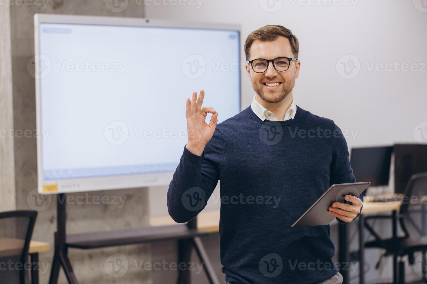 Professional businessman gesturing okay while using tablet, standing in contemporary workplace with confident demeanor photo