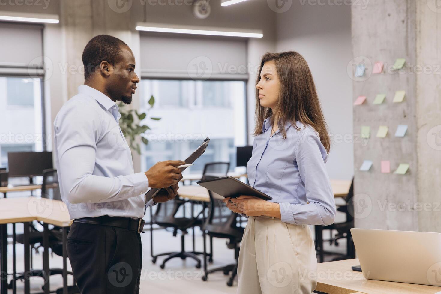 Businessman and businesswoman engaging in a work discussion in a modern office, utilizing a tablet and clipboard for effective collaboration photo