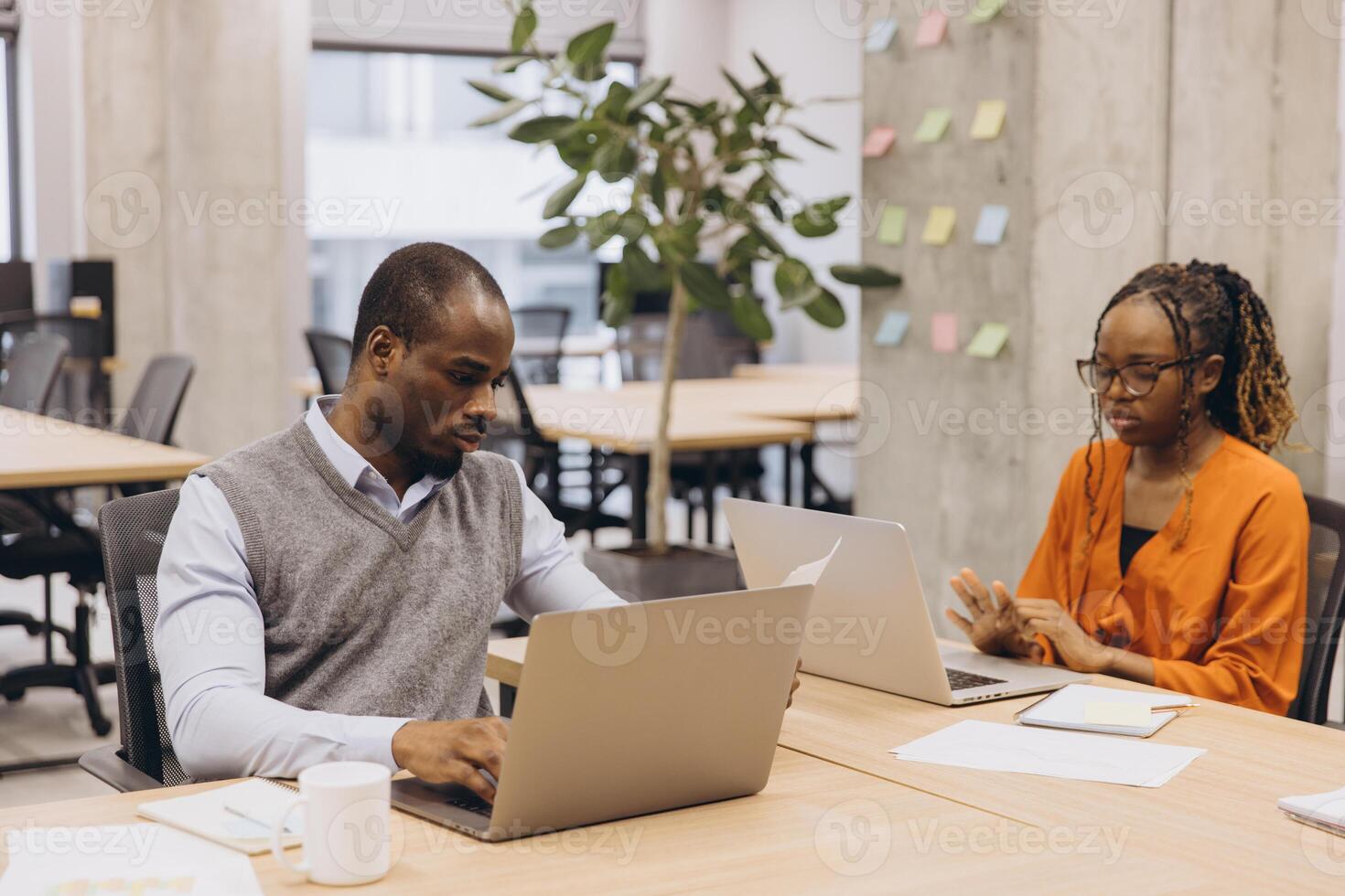 Two African American business people sitting at desks in a modern office, working on laptops and analyzing documents photo