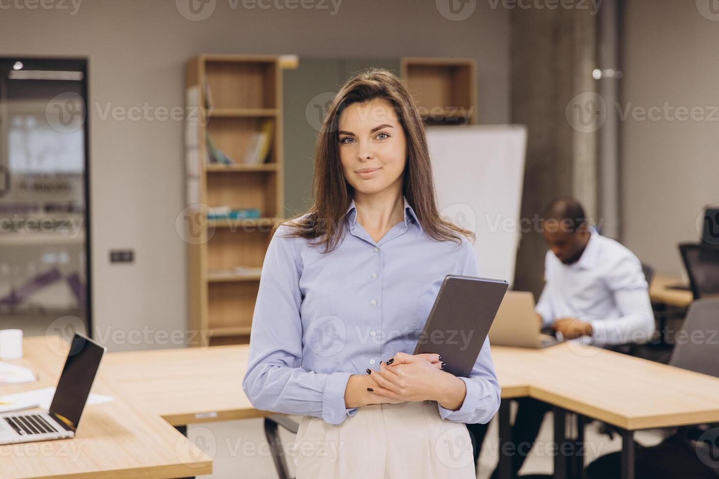 Professional female executive using tablet while colleagues collaborate in contemporary workplace, illustrating corporate innovation photo