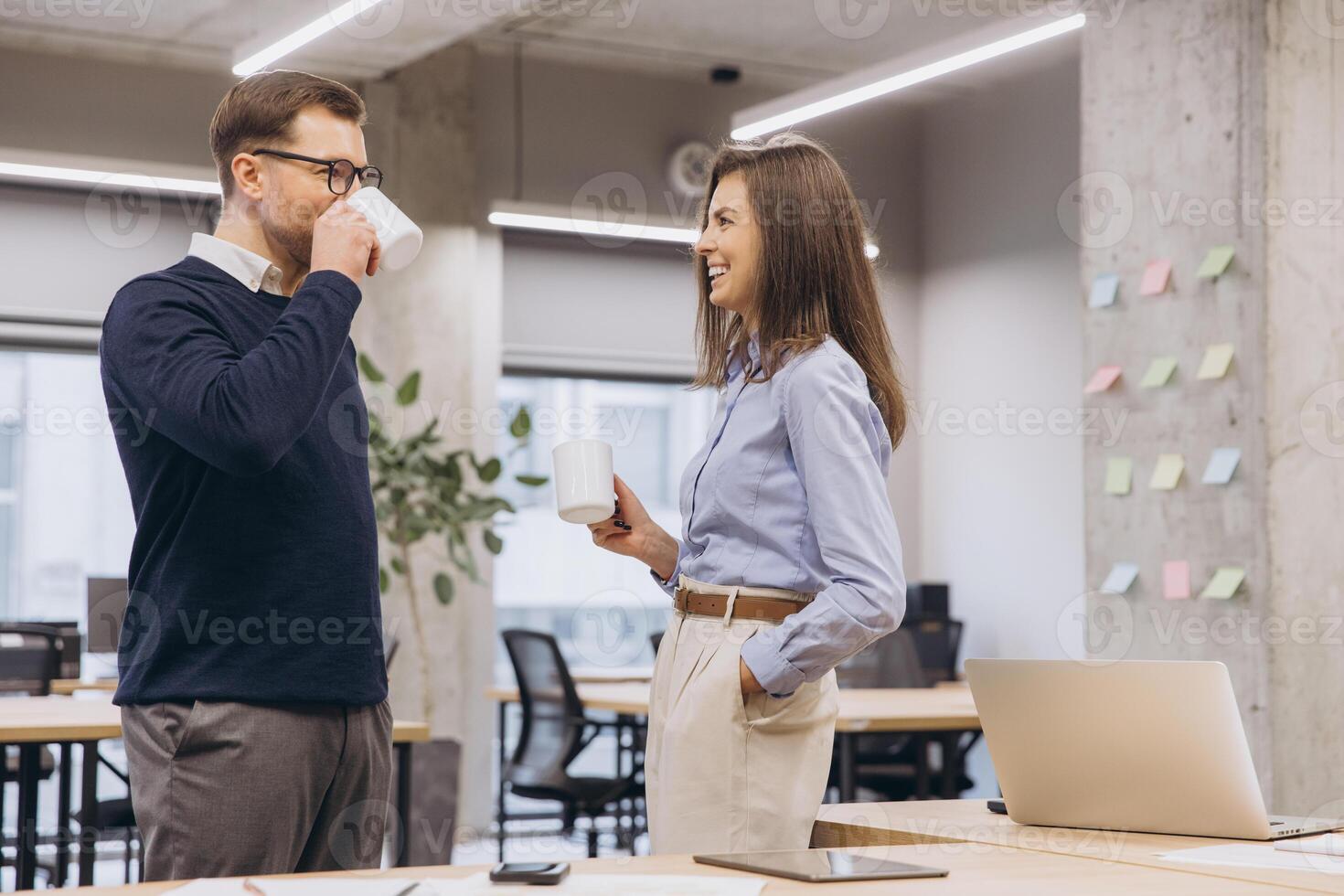 Colleagues drinking coffee and conversing near large windows, sharing ideas in contemporary workplace with natural light streaming inside photo