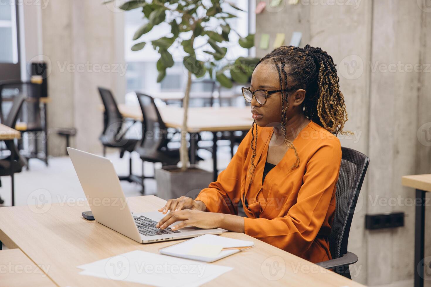 Professional African American female focusing on laptop task, working in bright, minimalist office with clean design and expansive windows photo
