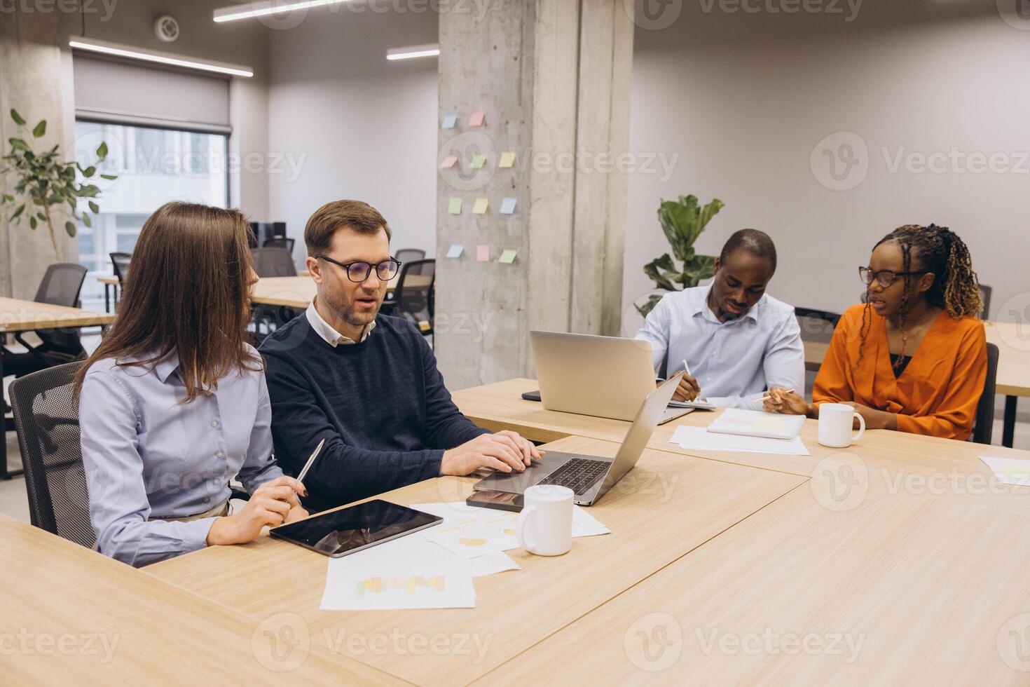 Four colleagues working together on a project, using laptops and tablets, sharing ideas and strategies in a bright open space photo