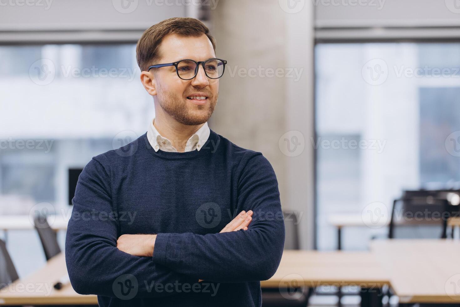 Confident businessman standing with crossed arms, radiating professional demeanor inside modern workspace with clean design photo