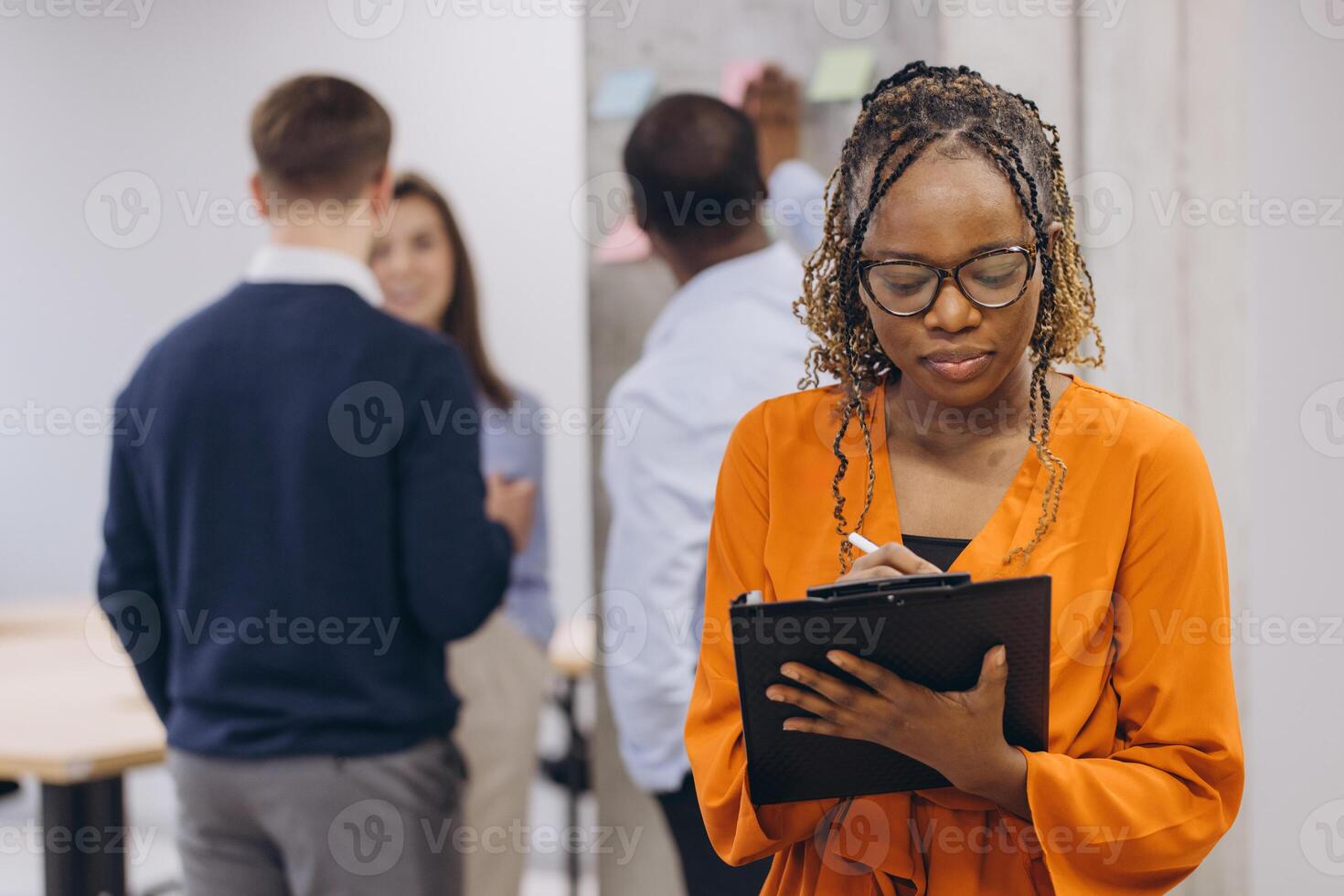 African american businesswoman holding a folder, business professionals engage in collaborative work, with a focus on teamwork and communication in a contemporary office environment photo