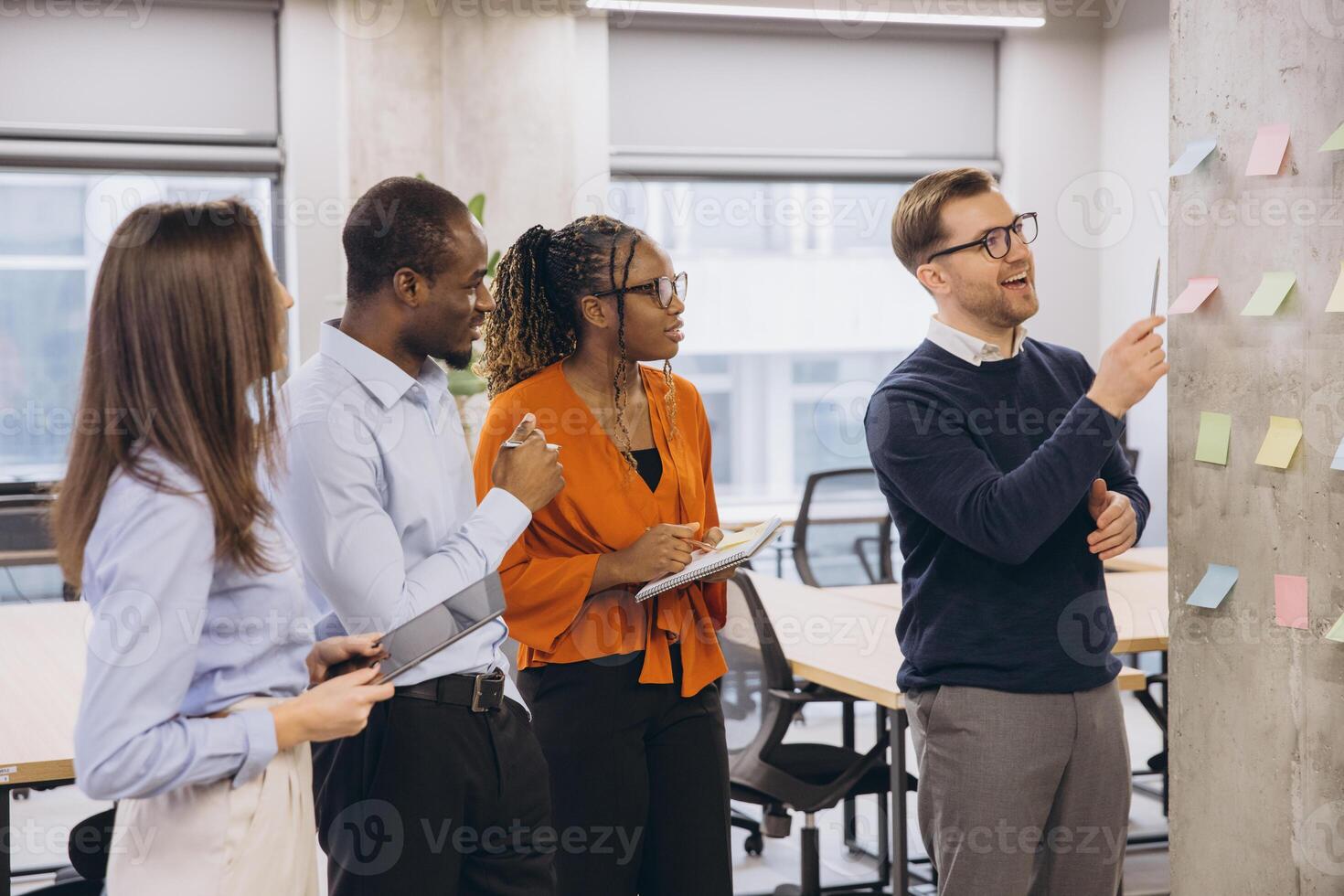 Diverse businesspeople brainstorming and discussing ideas using colorful sticky notes on a wall in modern office photo