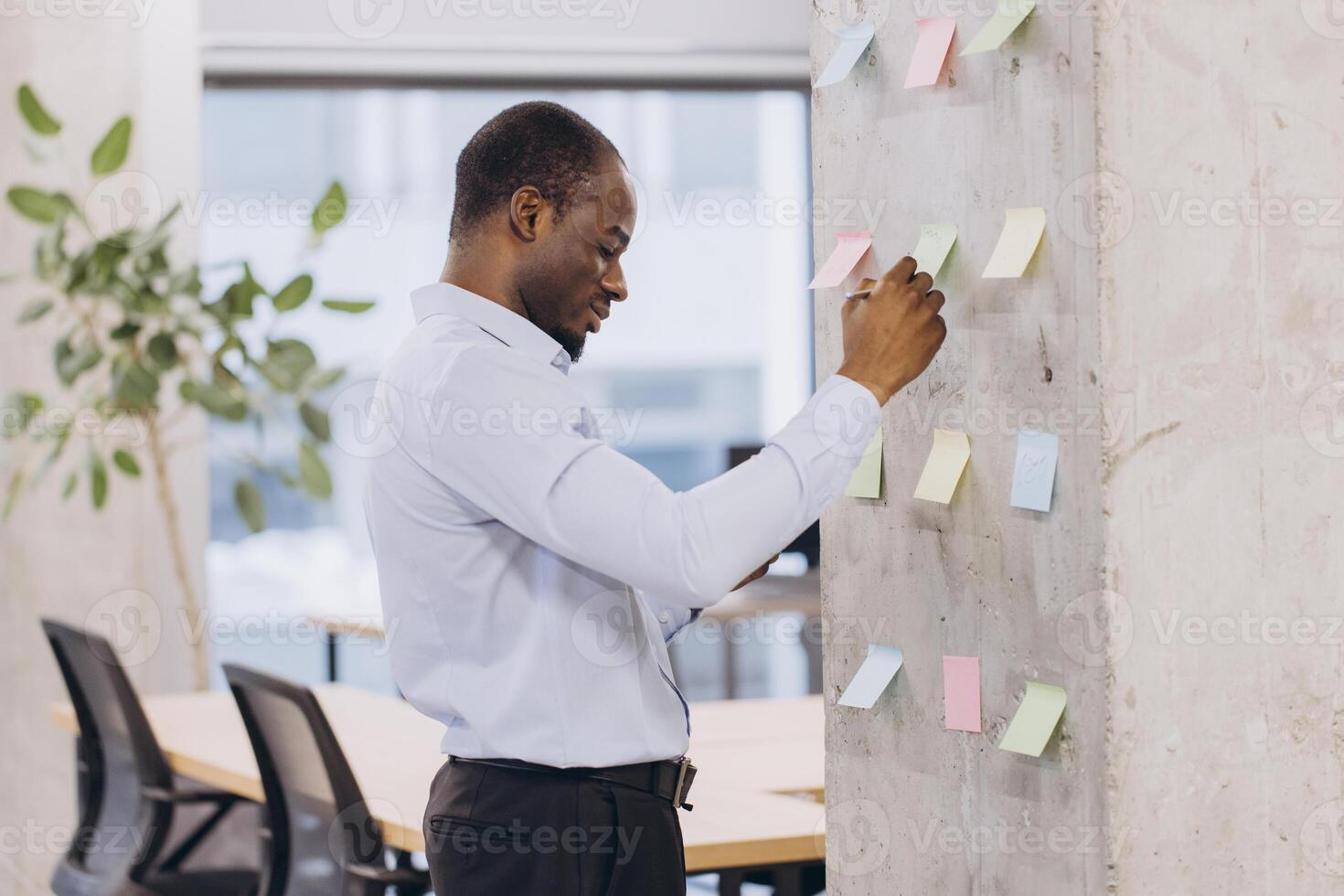 African american businessman organizing tasks with colorful sticky notes on a wall in a modern office, focusing on planning and strategic ideas photo