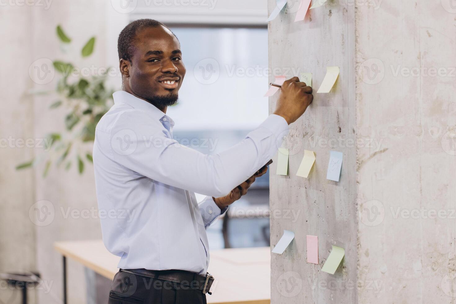 African american professional arranging colorful sticky notes on concrete wall, expressing collaborative planning and creative strategy in contemporary workspace photo