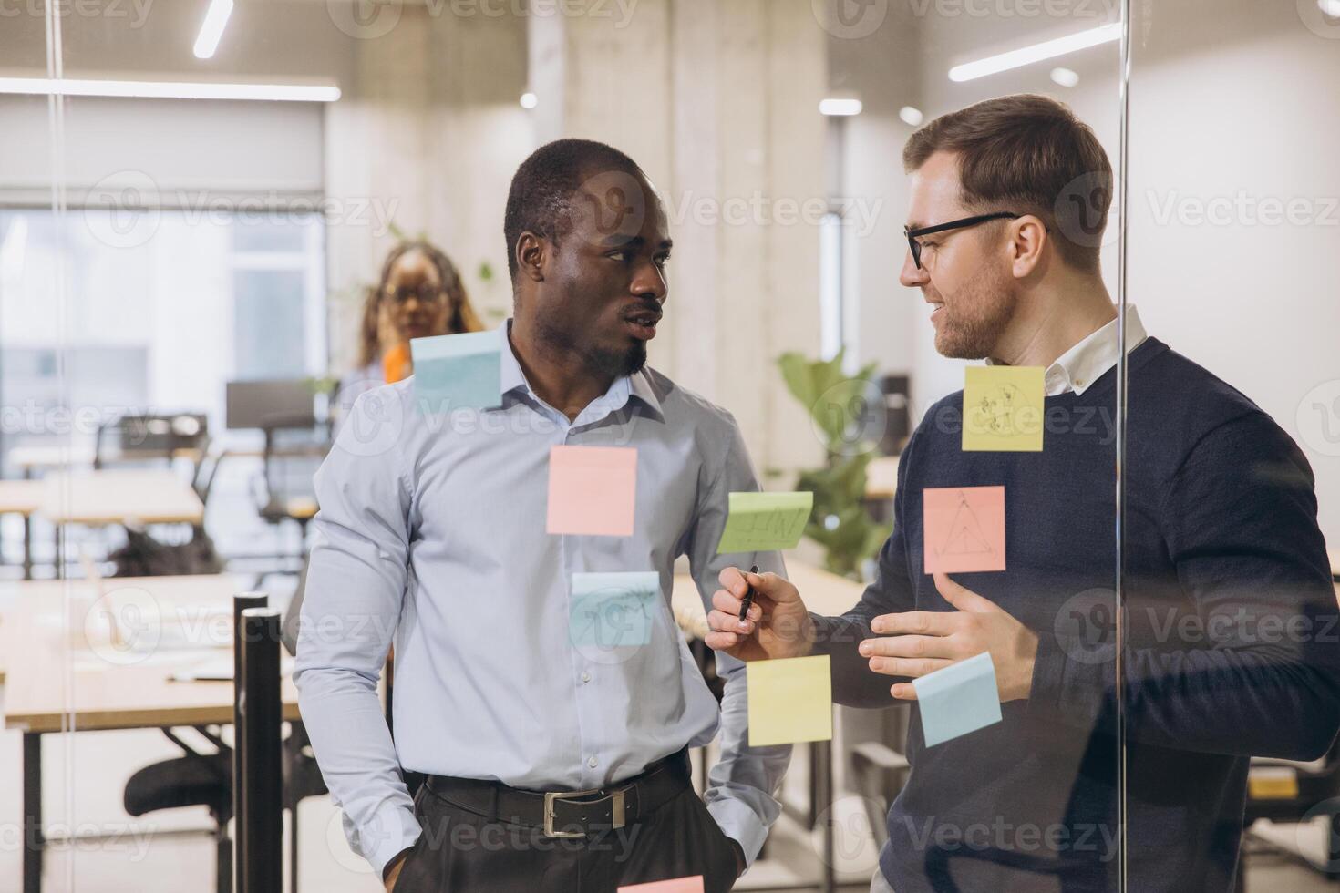 Two business professionals discussing ideas in a contemporary office environment, surrounded by colorful sticky notes on a glass wall photo