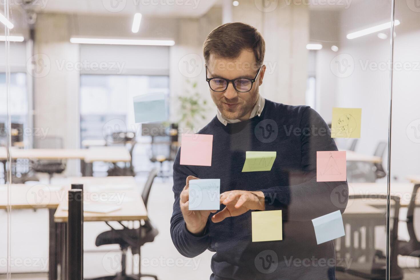 Professional man using colorful sticky notes on glass wall in modern office, planning and organizing tasks for a project photo