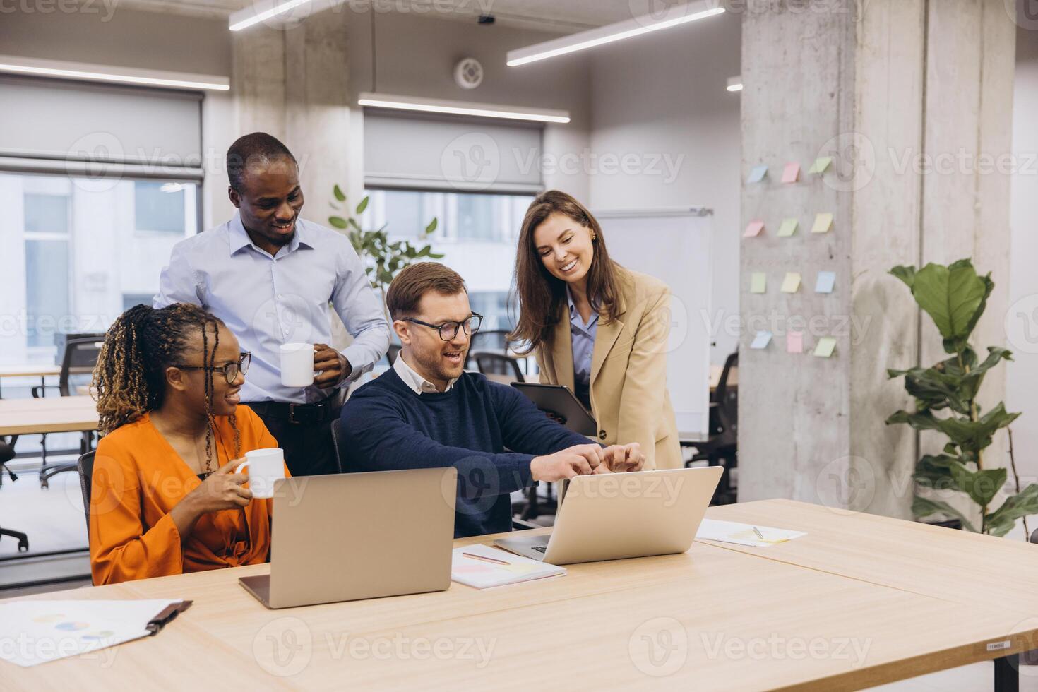 Diverse professionals discussing project details while leaning over laptop, collaborating in modern workplace setting with shared focus and creative energy photo