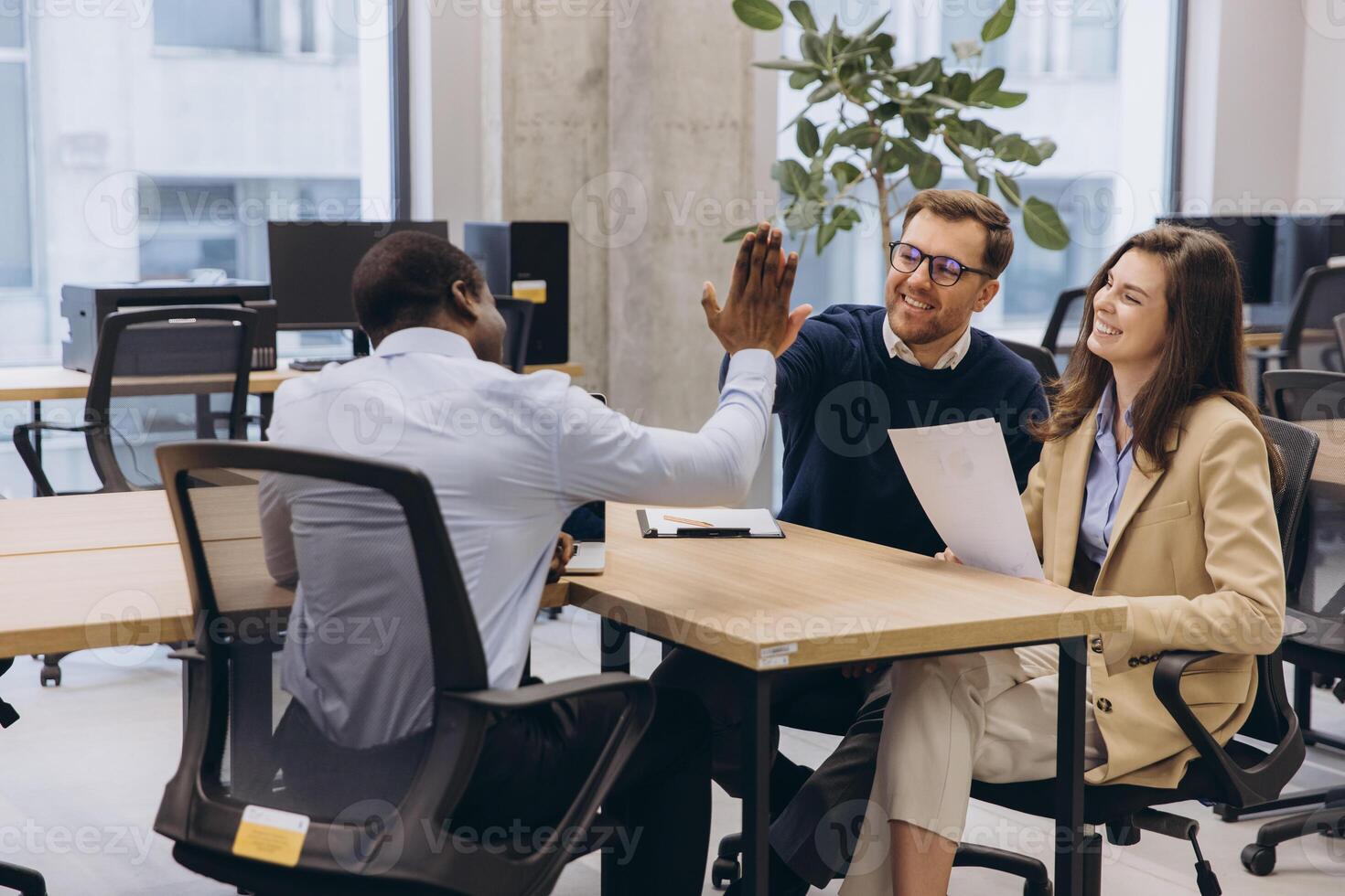 Diverse business team in a modern office environment celebrating success with a high five, showcasing teamwork and collaboration in a professional setting photo