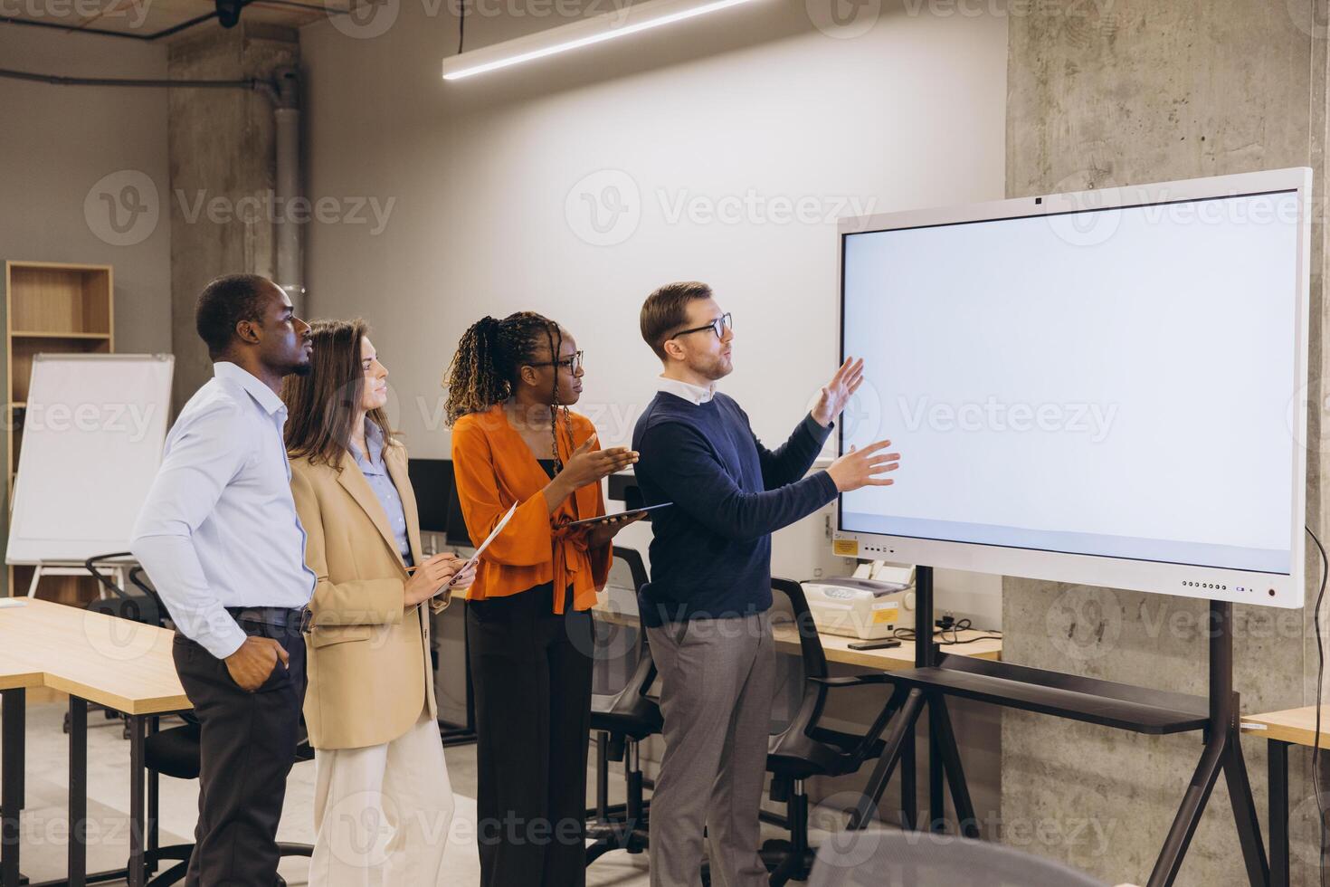 Diverse group of professionals engaging in a collaborative discussion around a large digital screen in a modern office setting photo