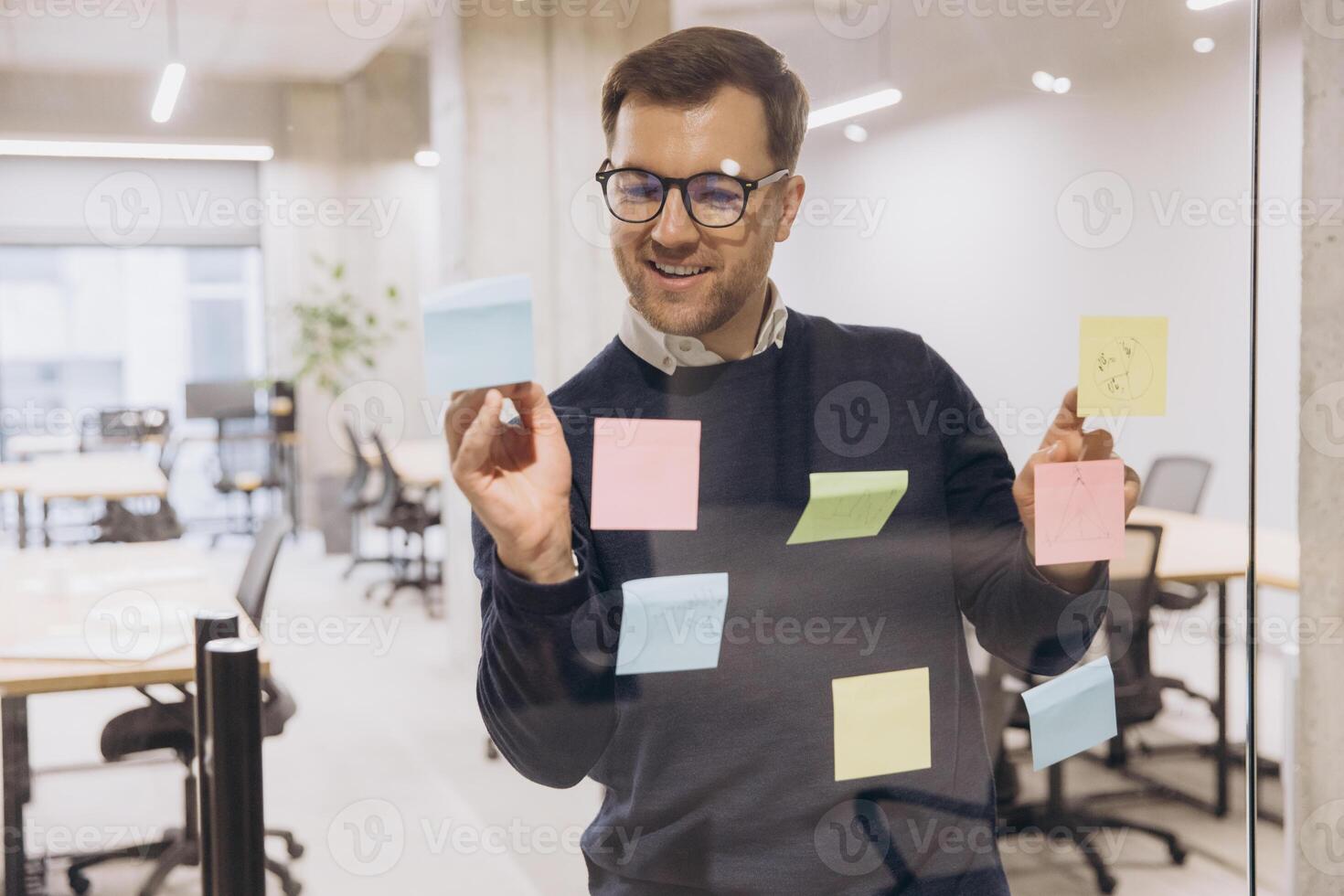 Business professional brainstorming ideas using colorful sticky notes on glass wall in modern office environment with open workspace photo