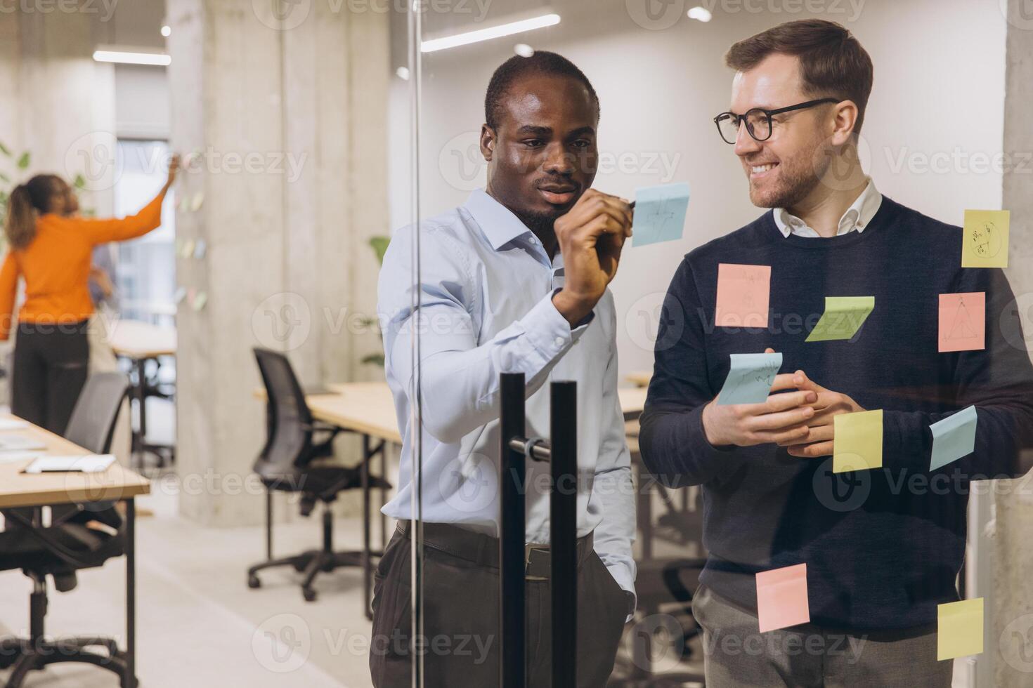 Two professional men discussing ideas with sticky notes on a glass wall in a contemporary office, promoting teamwork and innovation photo
