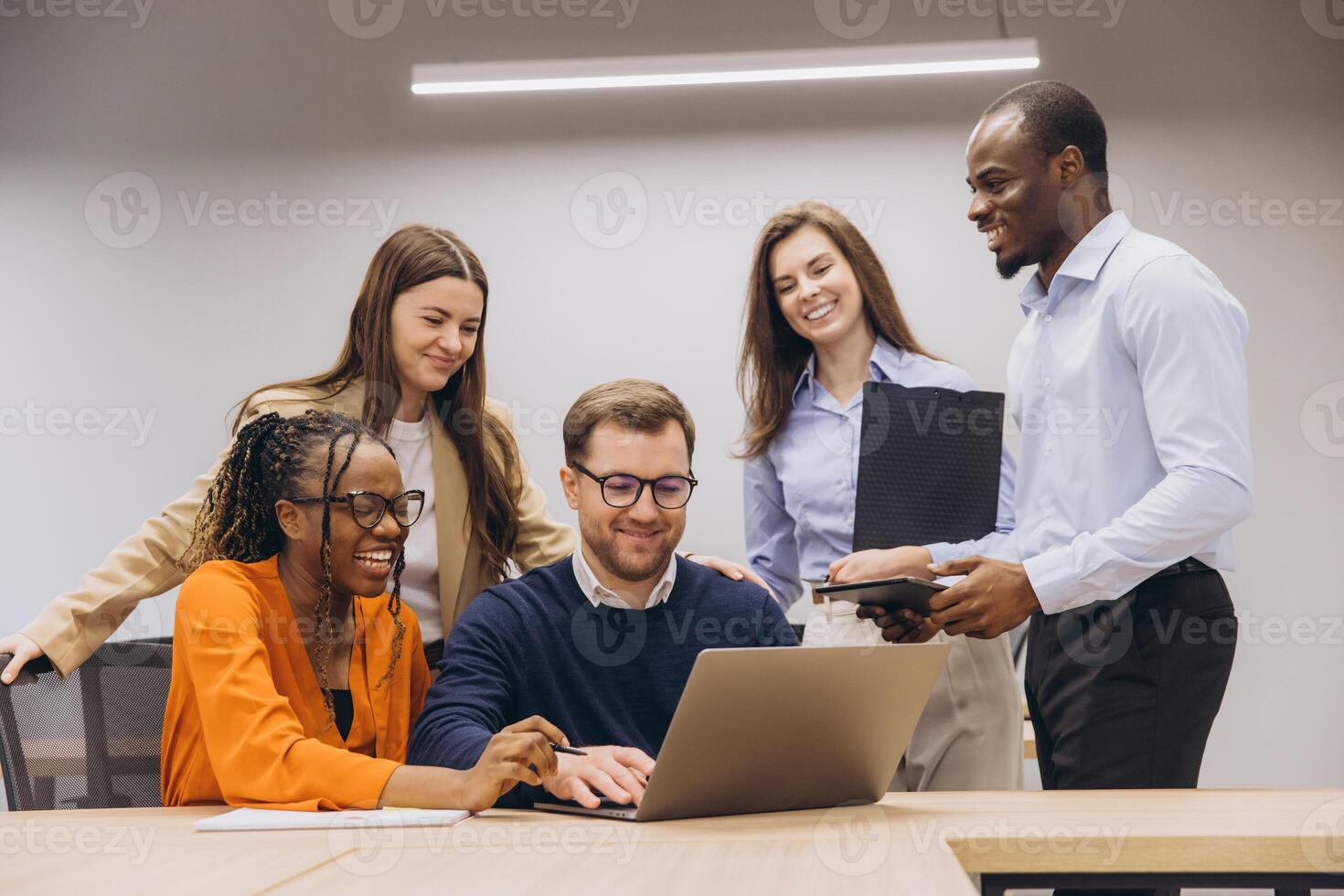 Professional team collaborating around laptop, displaying cultural diversity and teamwork in modern office environment photo
