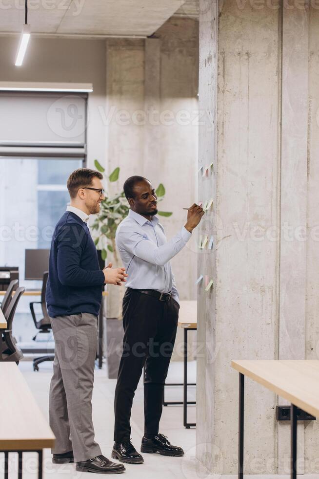 Professionals collaborating, writing ideas on sticky notes, sharing innovative thoughts in bright, contemporary office environment photo