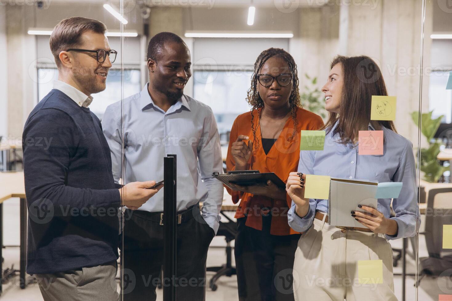 Diverse businesspeople brainstorming near whiteboard, sharing ideas with laptops, digital tablets, collaborative workspace environment photo