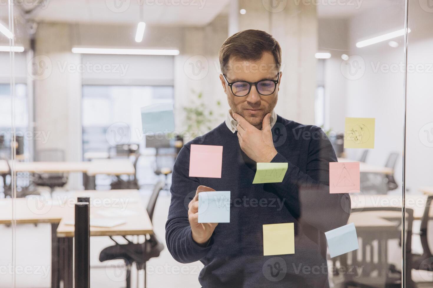 Businessman analyzing ideas on colorful sticky notes in a modern office setting, reflecting on strategic planning and innovation photo