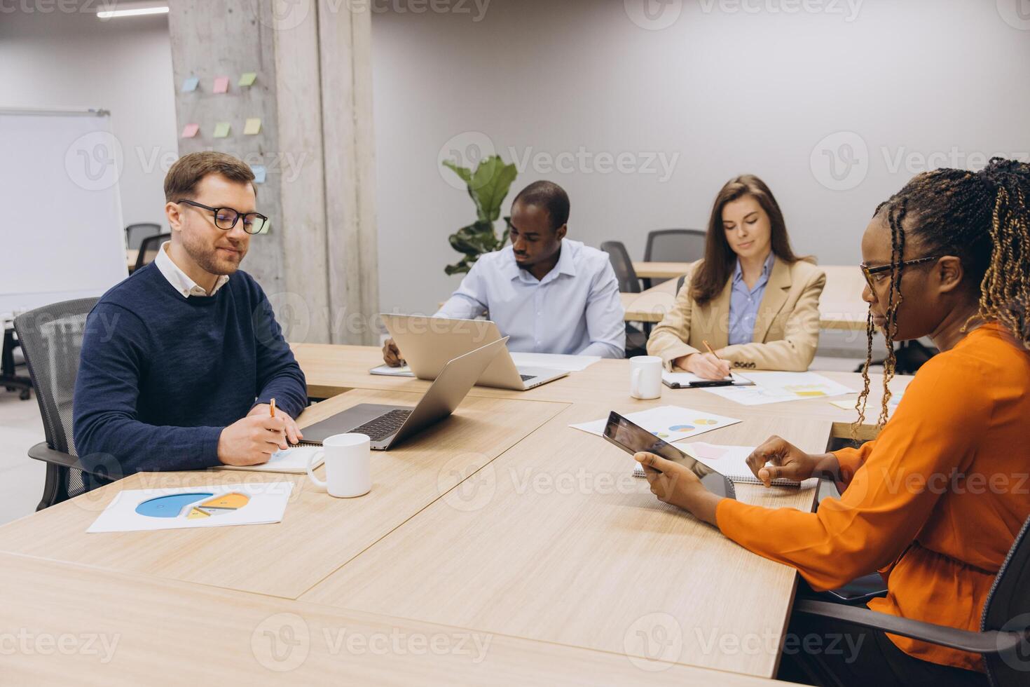 Diverse group of professionals engaged in a collaborative business meeting, using laptops and tablets, discussing charts and data in a modern office photo