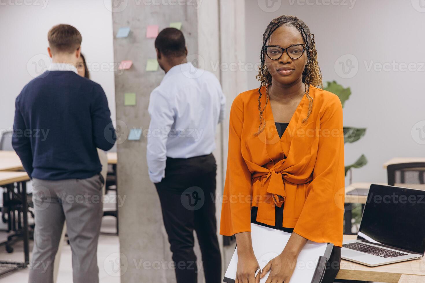 African american businesswoman holding a folder, diverse group of professionals engaged in discussion and planning in a modern office environment, showcasing teamwork and innovation photo