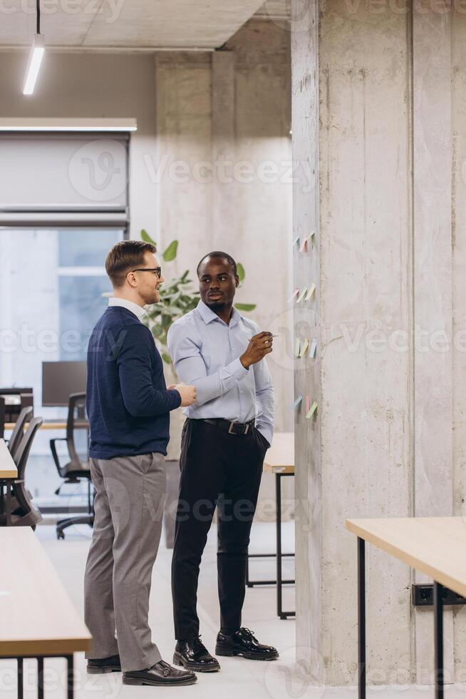 Two business professionals engage in a discussion, brainstorming ideas on a concrete wall in a contemporary office setting with natural light photo