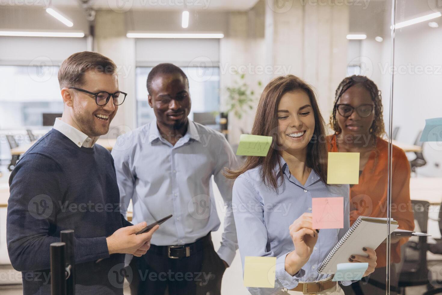 Business professionals collaborating, placing colorful sticky notes on glass wall during innovative team brainstorming meeting photo