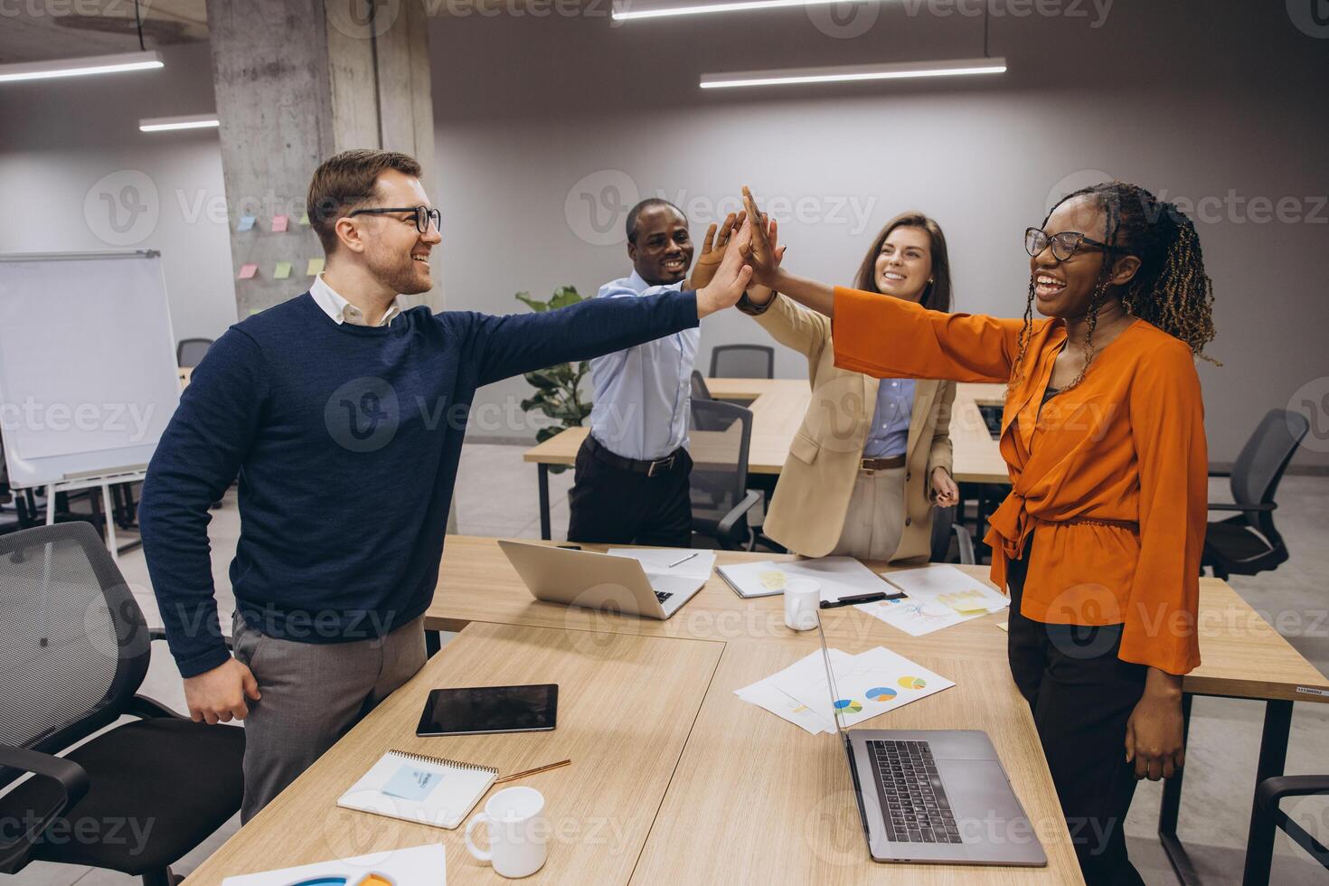 Diverse group of business professionals high fiving in a modern office setting, symbolizing teamwork, collaboration, and success in a corporate environment photo