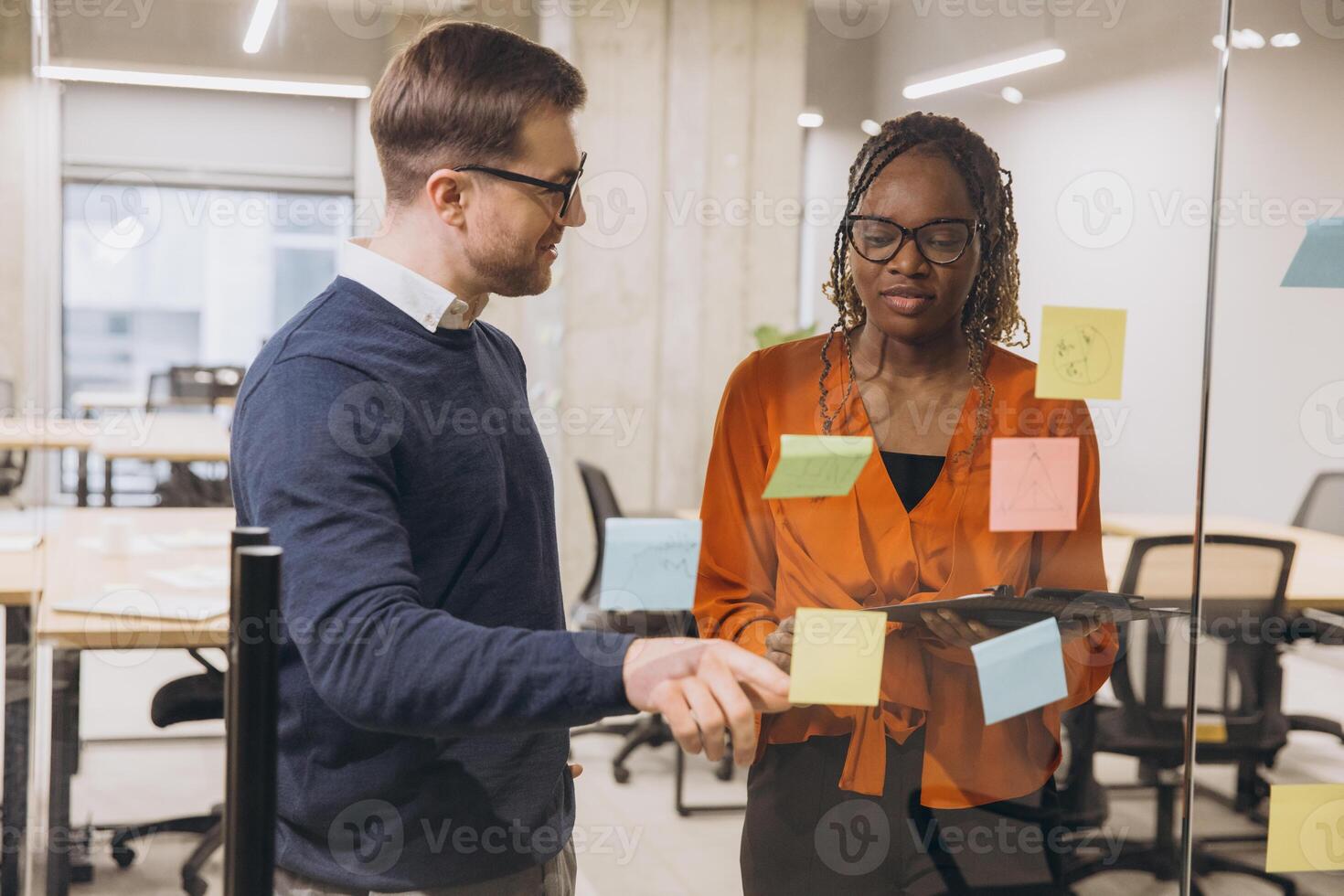 Creative professionals collaborating, writing ideas on sticky notes against glass wall in modern workspace, sharing innovative strategies photo