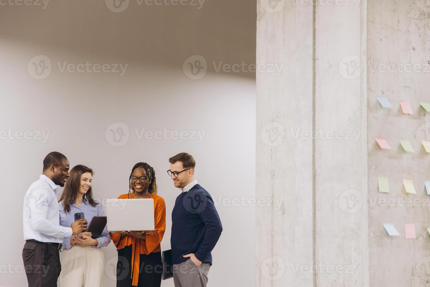 Business team collaborating, using digital devices near concrete wall, brainstorming with colorful sticky notes, modern workspace environment photo