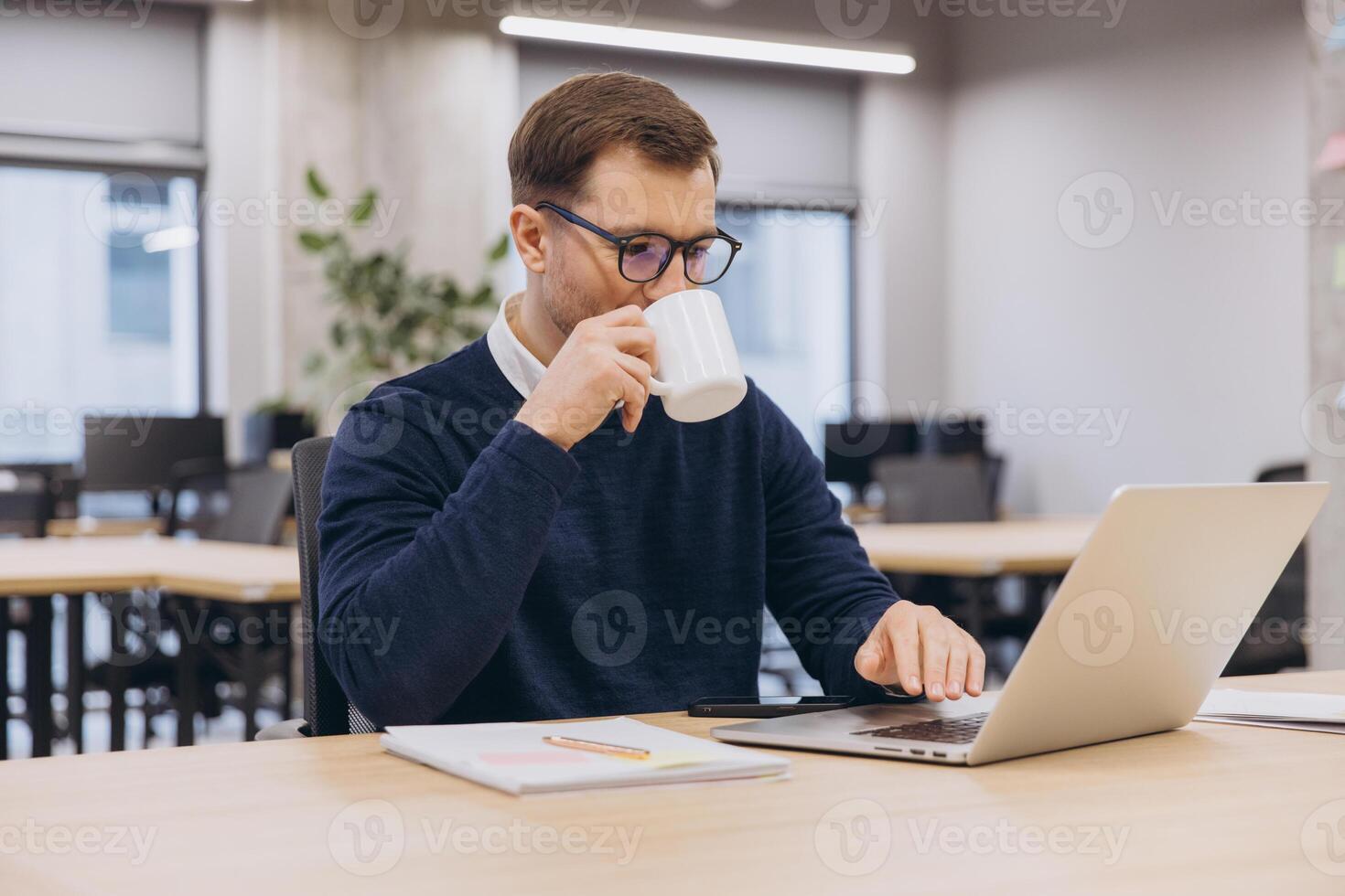 Professional working, sipping coffee while typing on laptop in modern shared workspace photo