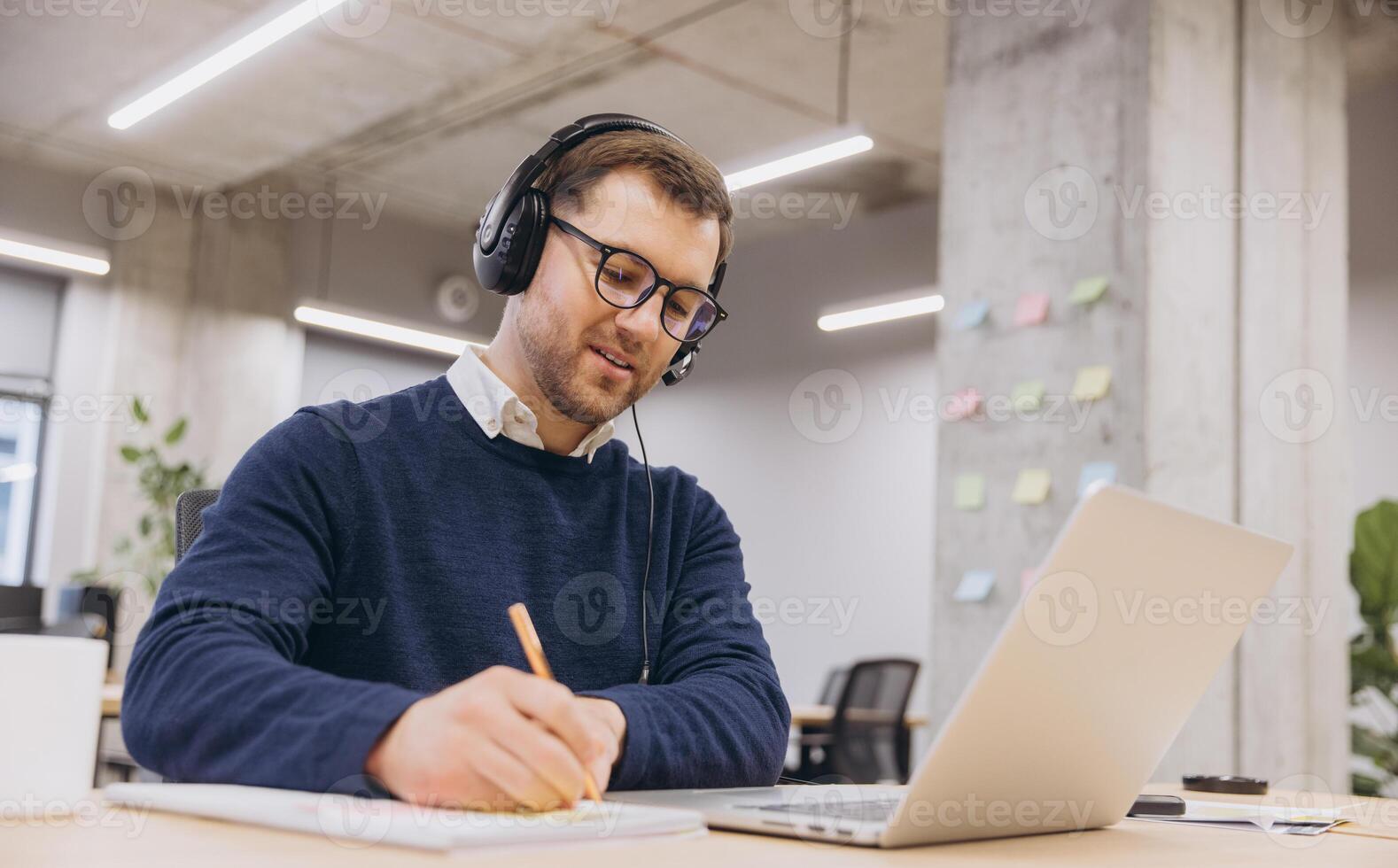 Professional employee participating in virtual conference, typing notes on laptop within contemporary, tech enabled work environment photo