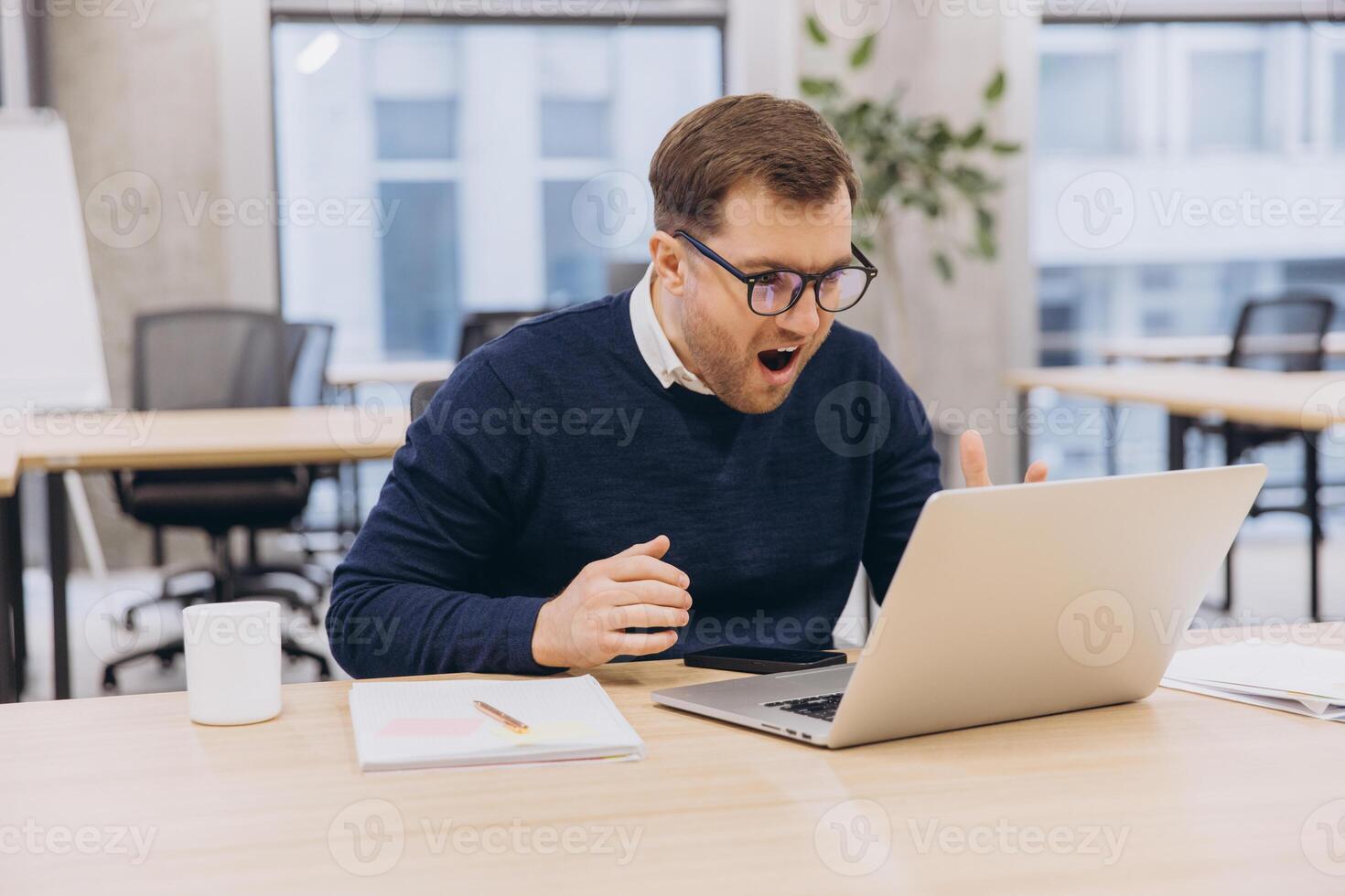 Surprised businessman looking at laptop in office with shocked facial expression, receiving unbelievable news photo