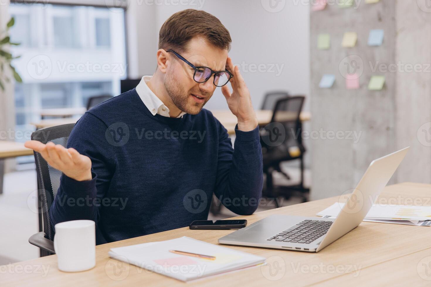Stressed professional experiencing headache, massaging temples while working on laptop, showing workplace fatigue and mental strain photo