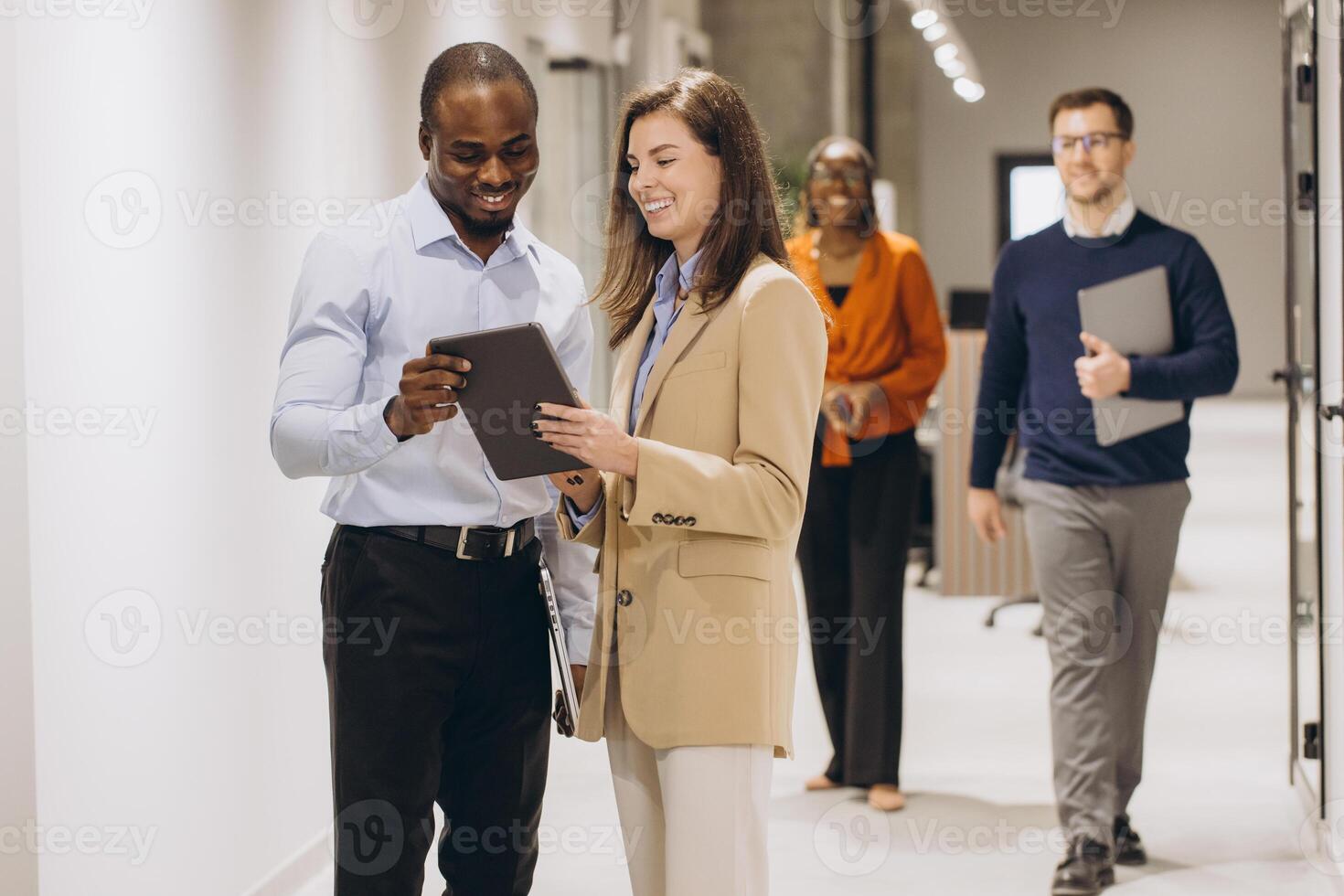 Business colleagues using a digital tablet while walking through a busy office corridor, discussing work related matters photo