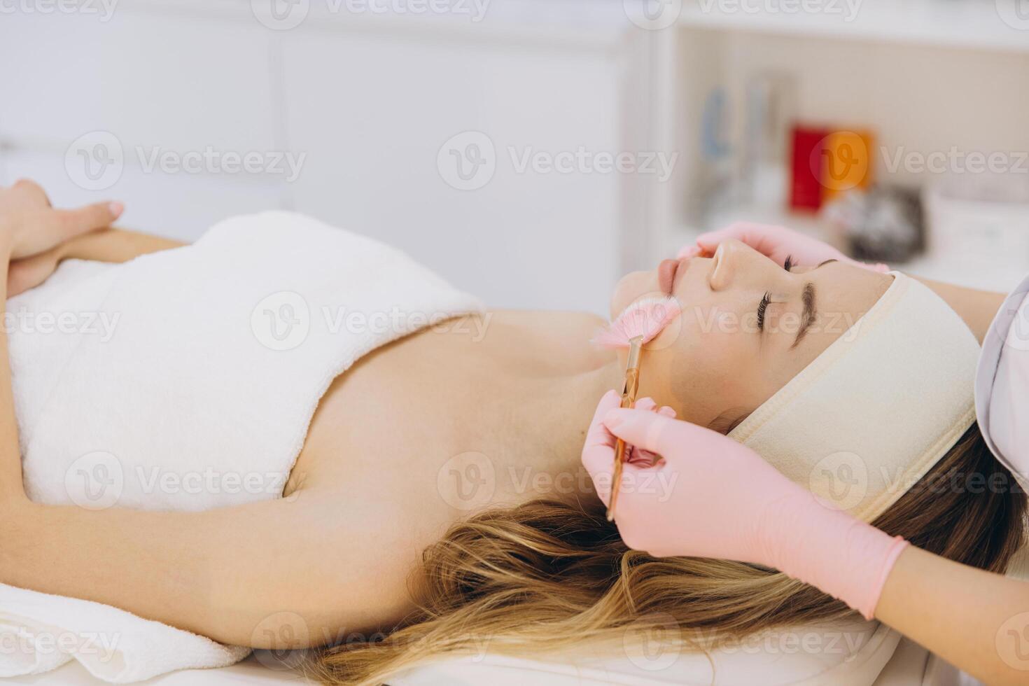 Beautician applying makeup carefully on female client during professional skincare treatment photo