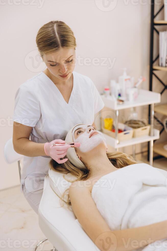 Skilled cosmetologist applies a facial mask to a client in a spa setting, emphasizing skincare and relaxation in a serene environment photo