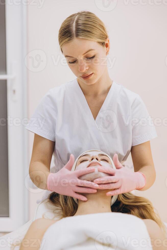 Professional beautician gently massaging client's face, applying soothing facial mask during relaxing spa treatment photo