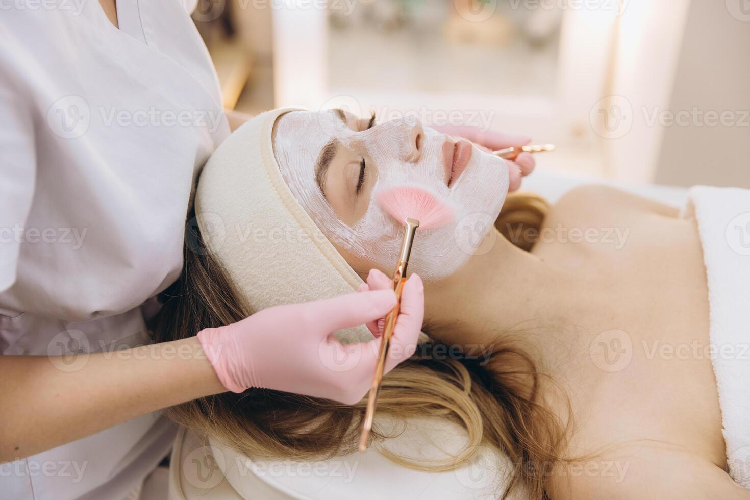 Cosmetologist applies a facial mask using brushes, focusing on skincare and relaxation in a serene spa environment photo