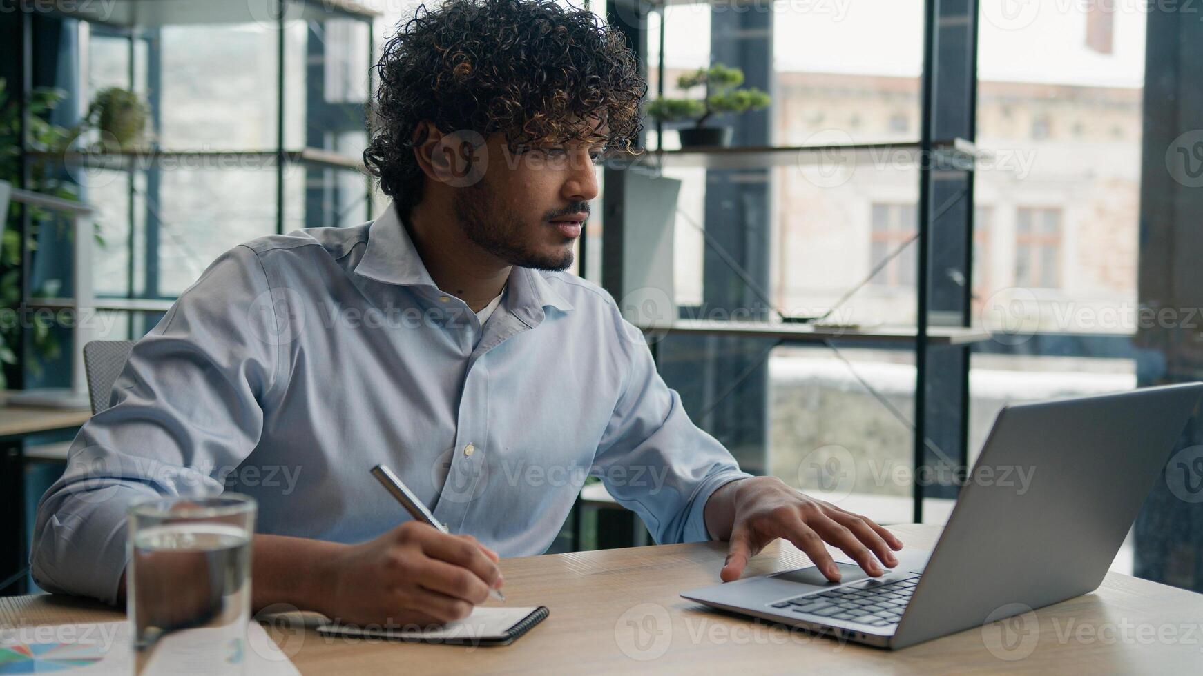 Indian Arabian man accountant writer business entrepreneur businessman write notes in notebook latino guy writing ideas report paperwork on office table studying online with laptop educational course photo