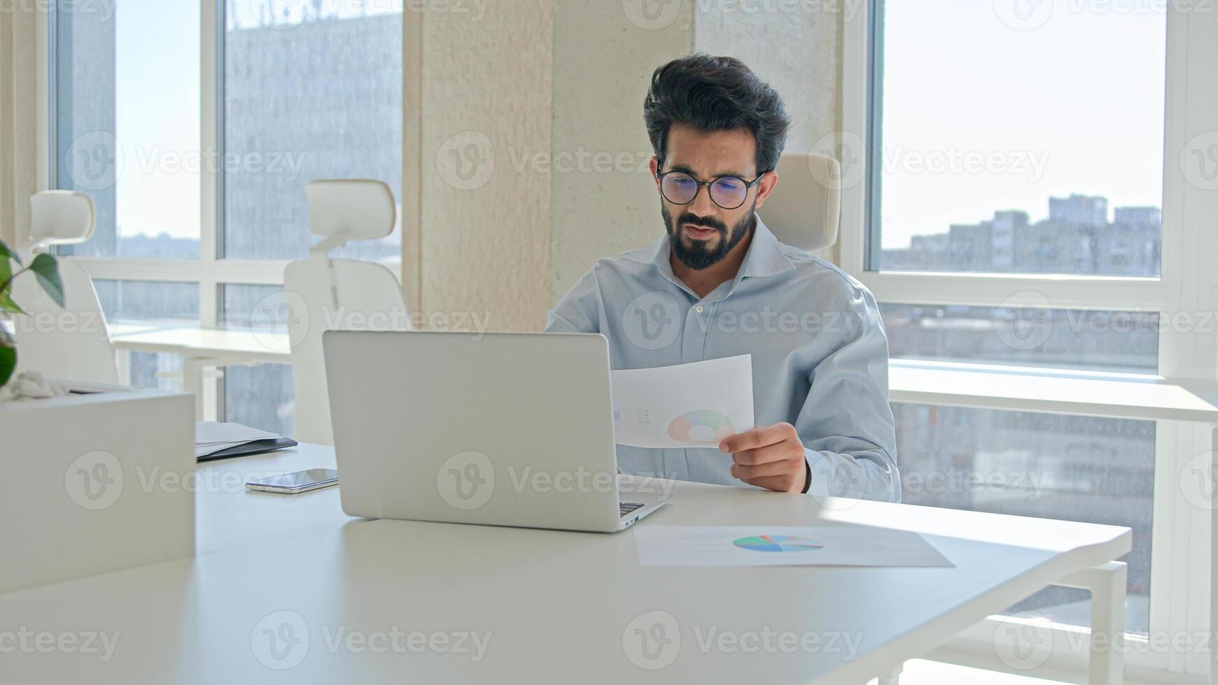 Arabian Indian man muslim male businessman entrepreneur professional executive worker manager working with laptop in office check information financial graphs read papers business documents paperwork photo